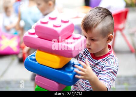 Carino ragazzo giocando con il giocattolo edili blocchi colorati. Il capretto con faccia felice giocando con mattoni di plastica. Plastica giocattolo di grandi dimensioni. Foto Stock