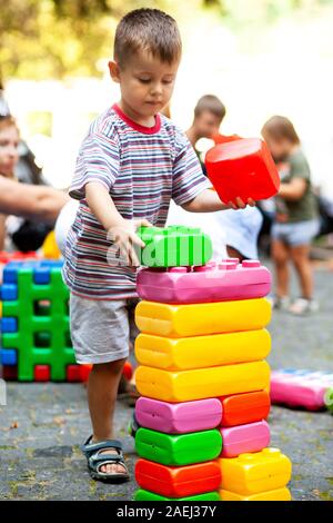 Carino ragazzo giocando con il giocattolo edili blocchi colorati. Il capretto con faccia felice giocando con mattoni di plastica. Plastica giocattolo di grandi dimensioni. Foto Stock