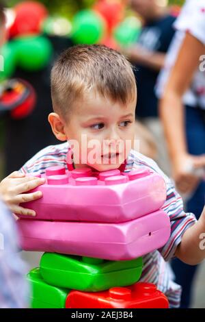 Carino ragazzo giocando con il giocattolo edili blocchi colorati. Il capretto con faccia felice giocando con mattoni di plastica. Plastica giocattolo di grandi dimensioni. Foto Stock