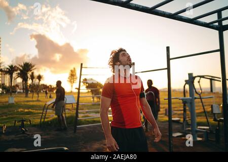 Giovane sportivo da uomo con gli auricolari nelle orecchie guardando il Monkey bar per fare esercizio in palestra park - Uomo motivare se stesso a fare esercizi Foto Stock