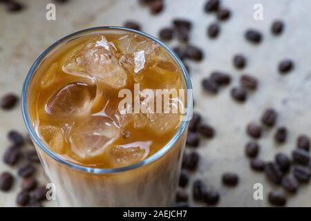 Dettaglio di un bicchiere di caffè ghiacciato con il latte, la crema di latte con i fagioli in background Foto Stock