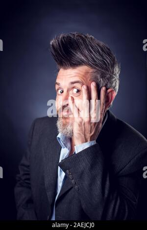 Un ritratto di divertenti uomo barbuto con iroquois indossare tuta che copre il volto con le mani. Le persone e le emozioni concetto Foto Stock