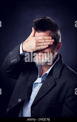 Un ritratto di divertenti uomo barbuto con iroquois indossare tuta che copre il volto con le mani. Le persone e le emozioni conce Foto Stock