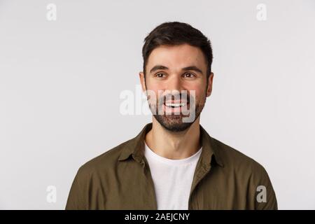 Guy check out interessanti eventi, guardando il piacere con il sorriso soddisfatto. Attraente uomo barbuto in cappotto su t-shirt, guardando a sinistra e smirking Foto Stock