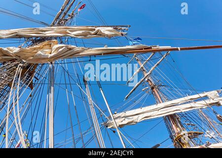 Alberi di legno di una vecchia nave a vela o alta nave con vele bianche arrotolate, bandiere e corde contro un cielo blu saturo. Foto Stock