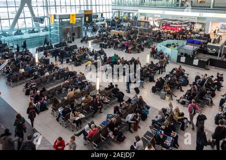 I passeggeri in un affollato aeroporto di Heathrow Terminal 5, Sala Partenze sedersi nelle panche in attesa dei loro voli. Foto Stock