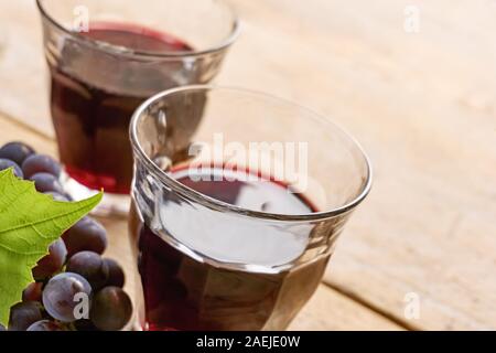 Informale due bicchieri di vino senza il piede su una tabella riempita con il vino rosso, blu uva e un verde foglia di uva. Angolo olandese shot con il fuoco selettivo. Foto Stock