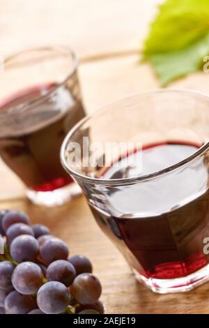 Informale due bicchieri di vino senza il piede su una tabella riempita con il vino rosso, blu uva e un verde foglia di uva. Verticale angolo olandese con il fuoco selettivo. Foto Stock