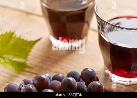 Informale due bicchieri di vino senza il piede su una tabella riempita con il vino rosso, blu uva e un verde foglia di uva. Inquadratura orizzontale con il fuoco selettivo. Foto Stock