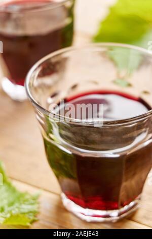 Informale due bicchieri di vino senza il piede e riempita con il vino rosso su una tavola e uva verde foglie. Colpo verticale con il fuoco selettivo. Foto Stock