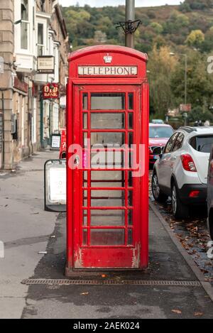 Matlock, Regno Unito - 6 Ottobre 2018: un vecchio bright British iconico telefono rosso nella casella al centro del telaio in una cittadina inglese Foto Stock