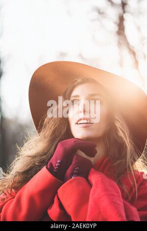 Ritratto di elegante ispirato la ragazza con i capelli lunghi che indossa ampia colmato cappello, guanti e ricoprire con lente effetto flare Foto Stock