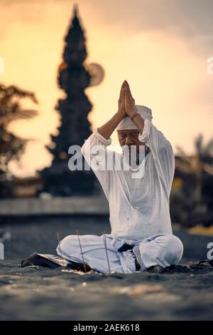 Bali, Indonesia - 10 DIC 2019: vecchio locale uomo balinese in meditazione vicino al mare. Concetto di pregare. Adulto pratica yoga sul Keramas sabbia nera beac Foto Stock