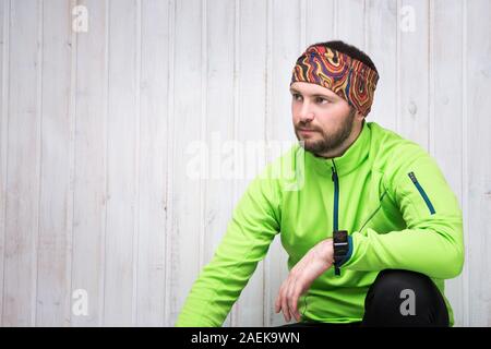 Giovane atleta di aspetto europeo in una giacca verde, guarda, pantaloni neri, si siede. Foto Stock