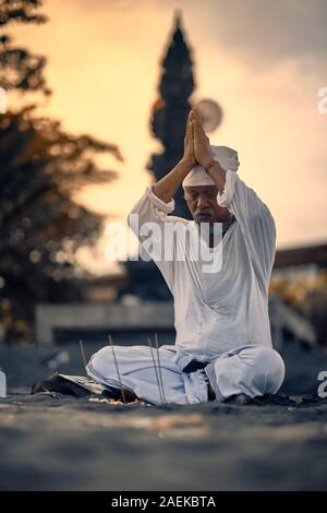 Bali, Indonesia - 10 DIC 2019: vecchio locale uomo balinese in meditazione vicino al mare. Concetto di pregare. Adulto pratica yoga sul Keramas sabbia nera beac Foto Stock