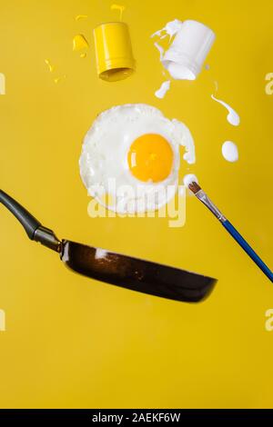 Uovo fritto e pan con barattoli di vernice rovesciato con gli spruzzi di vernice e un pennello levitare in aria. Foto Stock