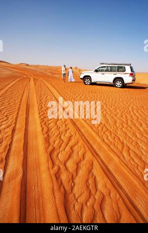 Tracce di pneumatici nella sabbia, turistico e beduini in piedi accanto al veicolo fuoristrada, safari nel deserto, deserto Rimal Wahiba Sands, Oman Foto Stock