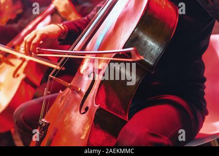 Concerto per violoncello con lo strumento vicino. Rosso sfondo vibrante al concerto rock Foto Stock