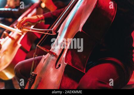 Concerto per violoncello con lo strumento vicino. Rosso sfondo vibrante al concerto rock Foto Stock