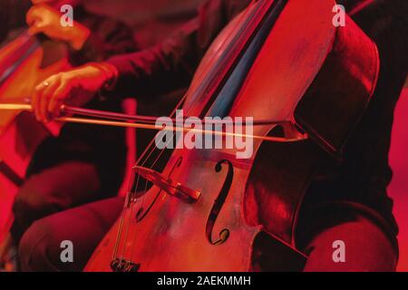 Concerto per violoncello con lo strumento vicino. Rosso sfondo vibrante al concerto rock Foto Stock