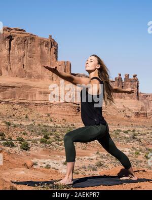 Giovane donna le pratiche yoga presso La Sal Mountains si affacciano nel Parco Nazionale di Arches nei pressi di Moab, Utah. Sullo sfondo sono il Courthouse Towers. Foto Stock