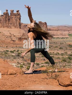 Giovane donna le pratiche yoga presso La Sal Mountains si affacciano nel Parco Nazionale di Arches nei pressi di Moab, Utah. Sullo sfondo sono il Courthouse Towers. Foto Stock