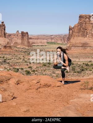 Giovane donna le pratiche yoga presso La Sal Mountains si affacciano nel Parco Nazionale di Arches nei pressi di Moab, Utah. Sullo sfondo sono il Courthouse Towers. Foto Stock
