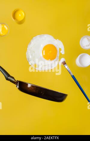 Un uovo fritto e una padella con le lattine di vernice e un pennello levitare in aria. Foto Stock