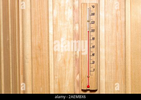 Retrò in legno in stile-termometro su una parete di tavole di colore giallo con una scala in gradi Celsius e un contrassegno rosso su un centinaio in la bathhouse durante il wellness Foto Stock