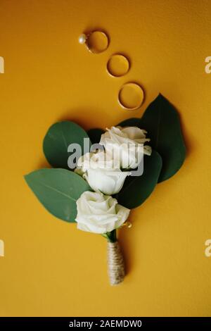 Scheda di matrimonio con una delicata rosa bianca e tre anelli di nozze su giallo, vista dall'alto Foto Stock