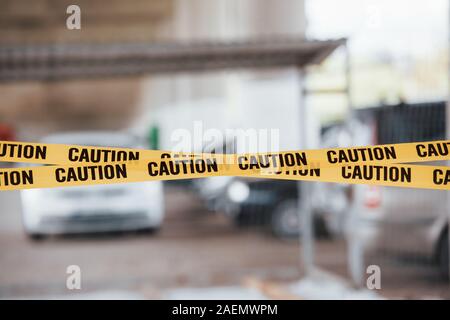 Sfondo sfocato. Spia gialla di attenzione nastro in prossimità del parcheggio auto al giorno. Scena del crimine Foto Stock