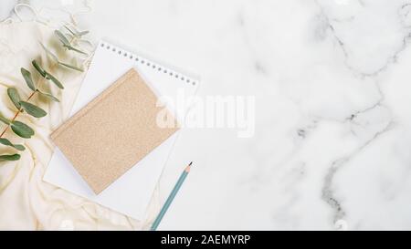 Home office desk tabella concetto. Il minimo piatto stile laici composizione con notebook carta, matita, eucalipto, donna sciarpa su marmo bianco dello sfondo. A Foto Stock