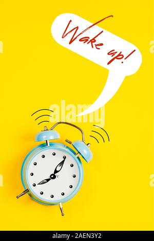 Blue orologio sveglia con grafica e testo Wake up su sfondo giallo Foto Stock