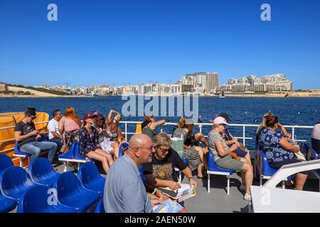 La Valletta, Malta - 17 Ottobre 2019: la Valletta i servizi di traghetto barca con un gruppo di persone, turisti sul ponte superiore con lo skyline di Sliema presso il Porto Marsamxett Harbo Foto Stock