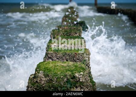 Sea Wave trasferite attraverso una groyne di legno accanto alla spiaggia. Foto Stock