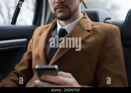 Ritratto di un giovane ragazzo di business. Un imprenditore corse in auto nel sedile del passeggero, parlando al telefono, utilizza uno smartphone. Business man in stylis Foto Stock