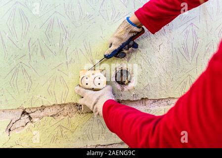 Mani di elettricista presa di riparazione sulla parete. Il vecchio impianto elettrico, ristrutturazione Foto Stock