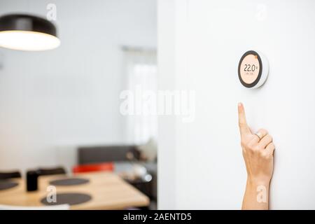 Round termostato intelligente con touch screen installato sulla parete con una mano cercando di raggiungere. Smart home regolamento riscaldamento concept Foto Stock