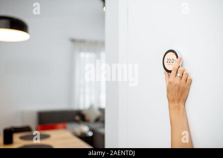 Round termostato intelligente con touch screen installato sulla parete con una mano cercando di raggiungere. Smart home regolamento riscaldamento concept Foto Stock