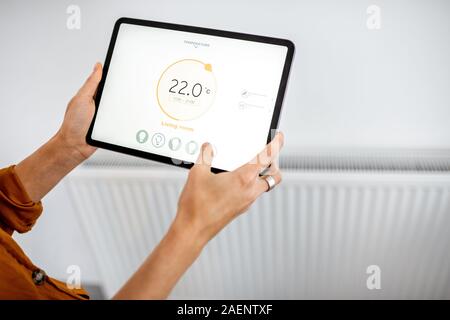 Controllare il radiatore riscaldamento la temperatura con una pastiglia, close-up di un radiatore con sullo sfondo. Concetto di una casa intelligente e applicazione mobile per la gestione di dispositivi intelligenti a casa Foto Stock