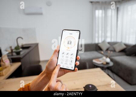 Tenendo un smartphone con ha lanciato il programma per la sicurezza in ambienti chiusi. Concetto di controllo e gestione della sicurezza domestica da un dispositivo mobile Foto Stock