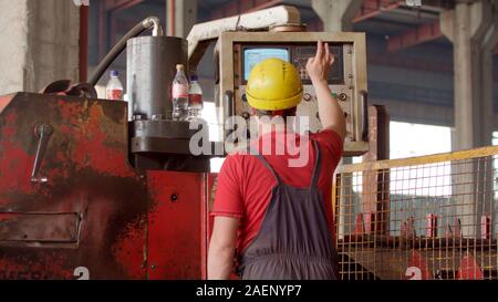 Un dipendente nel casco agendo una lavorazione metalli macchina che produce lamiera per ulteriore elaborazione. Tecnico meccanico operante progr Foto Stock