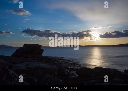 Impostazione di Sun a Elgol Beach con Black Cuillin Hills nella distanza sull isola di Skye in Scozia, nel Regno Unito nel mese di marzo - lunga esposizione Foto Stock