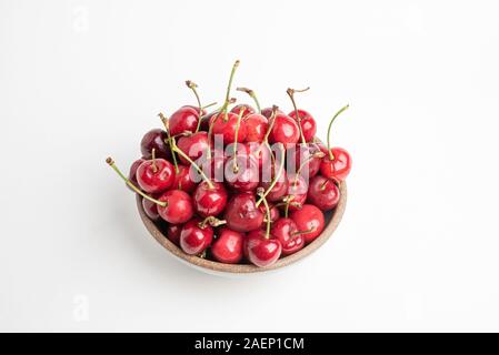 Un mazzetto di fresche ciliege rosse disposti e montati in rotondo piccolo recipiente di ceramica impostato su sfondo bianco. Foto Stock