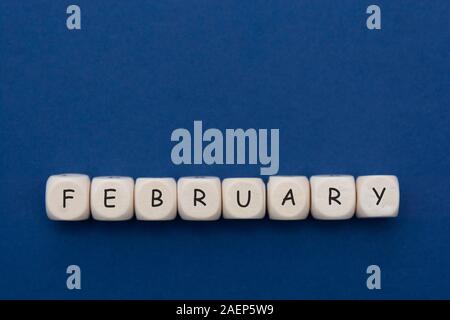 Febbraio scritto su blocchi di legno oltre il classico sfondo blu, isolato con copia spazio. Foto Stock