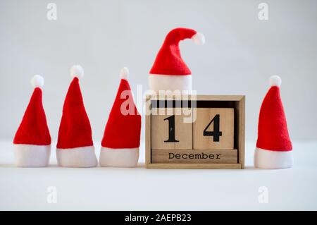 Cubo di legno che mostra calendario data 14 dicembre con piccoli cappelli di Babbo Natale su sfondo bianco. Calendario dell'Avvento, Natale sfondo, spazio di copia Foto Stock