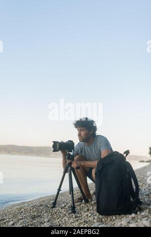 Giovane maschio fotografo sulla spiaggia per configurare il suo fotocamera su treppiede per star il servizio fotografico. Foto Stock