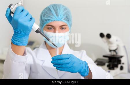 Donna scienziato facendo cadere i campioni provenienti da grandi pipetta per test su moderne attrezzature da laboratorio Foto Stock