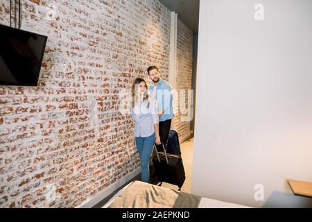 Coppia giovane a camera d'hotel. Vacanza per coppia adorabile. Coppia giovane di entrare nella camera di albergo insieme, tirando le loro valigie. Foto Stock