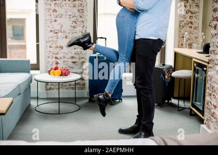 Immagine ritagliata di gambe di giovani amare giovane in abbigliamento casual spendere tempo romantico insieme, abbracciando nella stanza dell'hotel. Uomo Donna mantiene sulle mani. Foto Stock